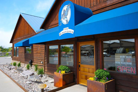 The Kingfisher store exterior with blue awning and wooden facade under a clear blue sky.