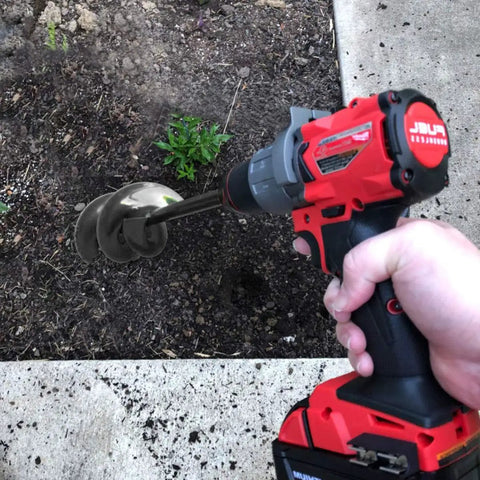 Hand holding drill with Garden Auger Drill Bit For Bulbs And Bedding Plants, 1.8 By 15 Inch, digging soil in garden bed.