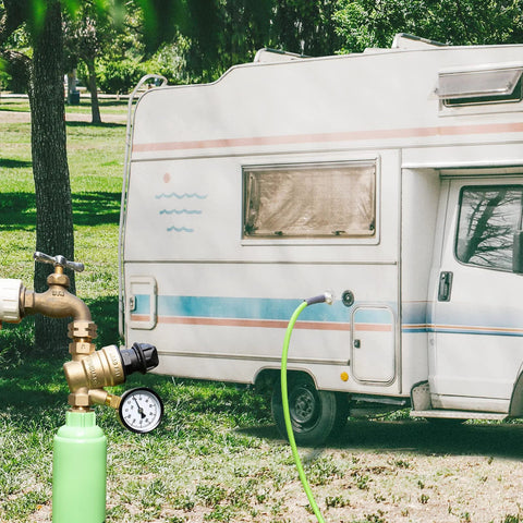 Brass RV water pressure regulator with gauge, installed on hose at the camper water inlet.