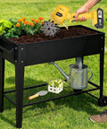 Person using Cordless 20V Tiller Cultivator For Gardening in elevated planter with flowers, ergonomic grip, 240 RPM power.