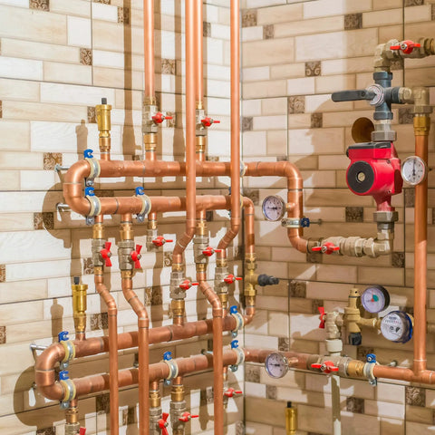 Front view of copper plumbing manifold with brass fittings, red valve handles, and gauges.