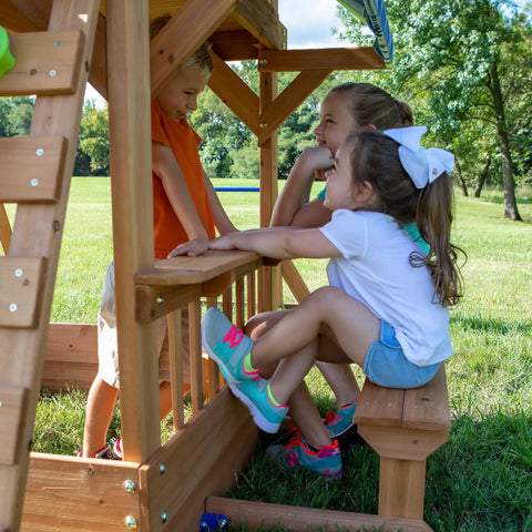Children playing at snack bar window of Beachfront Cedar Wood Swing Set With Wave Slide Elevated Deck Canopy Monkey Bars Rock Wall Ladder Shaded Picnic Area Snack Bar Window Belt Swings Trapeze Sandbox Playset For Kids.