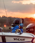 Angler on a boat holding a fish at sunset, using the Wally Marshall Signature Series Underspin Fishing Reel With All Metal Gears 2 Plus 1 Bearings 4 Point 3 To 1 Gear Ratio Reversible Handle Smooth Casting And Retrieval For Easy No Fuss Fishing.