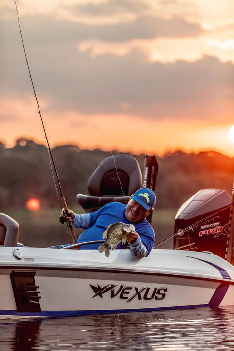 Angler on a boat holding a fish at sunset, using the Wally Marshall Signature Series Underspin Fishing Reel With All Metal Gears 2 Plus 1 Bearings 4 Point 3 To 1 Gear Ratio Reversible Handle Smooth Casting And Retrieval For Easy No Fuss Fishing.