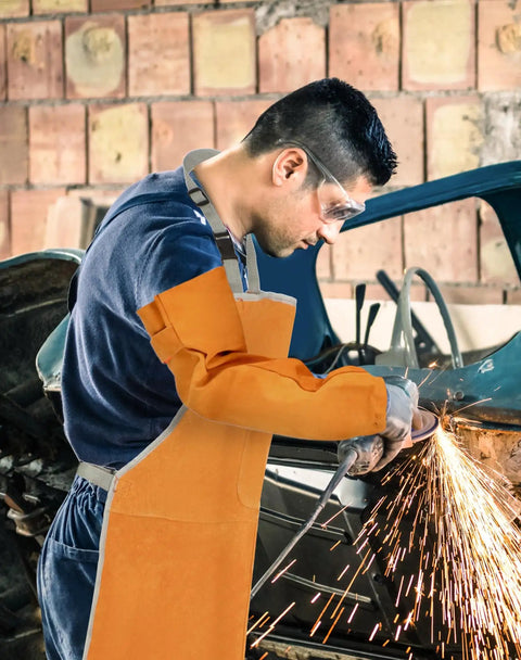 Welding Apron And Sleeves Set With Front Pockets For Heat And Flame Resistant Leather Shop Wear For Welders Blacksmiths Fireplace BBQ Gardening And Safety Bib Apron in use by a welder, sparks flying from grinding metal.