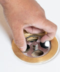 Hand using No Calk Shower Drain Wrench with brass and plastic construction; stainless steel core visible in a shower drain.