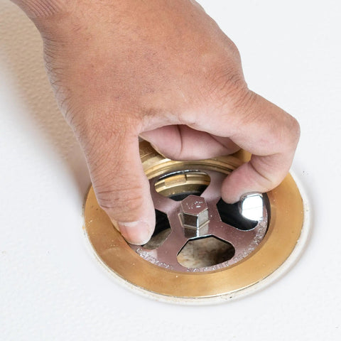 Hand using No Calk Shower Drain Wrench with brass and plastic construction; stainless steel core visible in a shower drain.