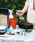 Person using Seed Storage Organizer Kit With 70 Slots, 20 Seed Envelopes, Label Cards, Funnel And Tweezer on stone table.