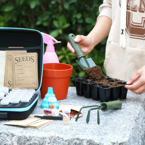 Person using Seed Storage Organizer Kit With 70 Slots, 20 Seed Envelopes, Label Cards, Funnel And Tweezer on stone table.