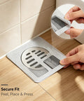80Pcs 4x4 Disposable Hair Drain Stickers Anti Blocking applied over a drain with a hand demonstrating secure fit.