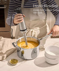 Heavy Duty Stainless Steel Immersion Blender With Kickass 600 Watt Motor And Turbo Switch blending soup in a pot on a kitchen counter.