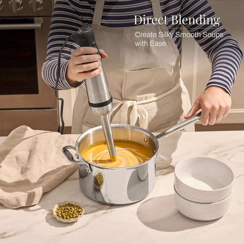 Heavy Duty Stainless Steel Immersion Blender With Kickass 600 Watt Motor And Turbo Switch blending soup in a pot on a kitchen counter.