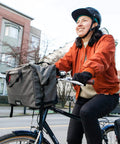 Woman cycling with 4 In 1 Dayliner Box Bag 20 Liter Water Resistant Rolltop on handlebars, urban setting, wearing helmet