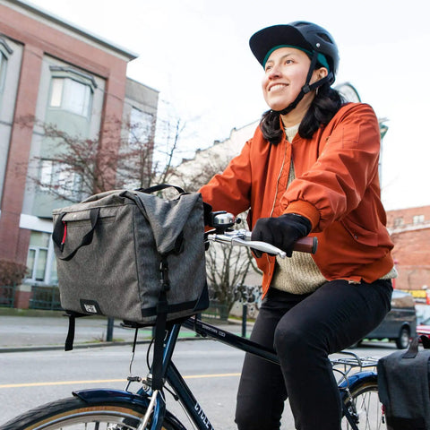 Woman cycling with 4 In 1 Dayliner Box Bag 20 Liter Water Resistant Rolltop on handlebars, urban setting, wearing helmet