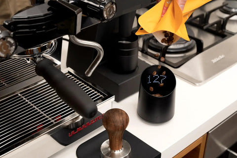 Subscale Digital Dosing Cup With LED Display Sleek Black Scale For Espresso Brewing next to espresso machine and tamper
