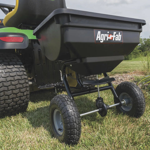 Tow Behind Broadcast Spreader With 85 Lb Capacity For Lawns, 10 Foot Spread, Covers Up To 14,000 Sq Ft, attached to a tractor.