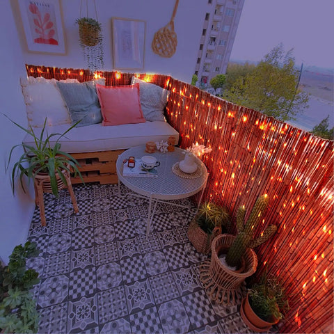 Outdoor balcony with brown reed fence roll privacy screen, decorated with lights, plants, and a cozy seating area, 4 ft by 16.4 ft.