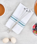 Stainless Steel Ball Whisk With Silicone Tips 10.5 Inch 24 Pack Non Scratch Dishwasher Safe Non Stick Silicone Ball Whisk For Cooking And Baking Great For Sauces And Gravies Kitchen Workhorse resting on a kitchen towel with ingredients.