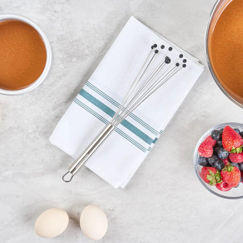 Stainless Steel Ball Whisk With Silicone Tips 10.5 Inch 24 Pack Non Scratch Dishwasher Safe Non Stick Silicone Ball Whisk For Cooking And Baking Great For Sauces And Gravies Kitchen Workhorse resting on a kitchen towel with ingredients.