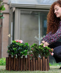Woman installing Burnt Wood Garden Fence Edging, 8 Inch Tall and 3.7 Foot Long, as decorative border for flower beds.