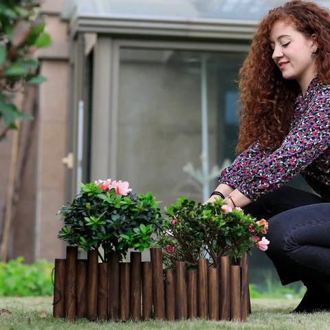 Woman installing Burnt Wood Garden Fence Edging, 8 Inch Tall and 3.7 Foot Long, as decorative border for flower beds.