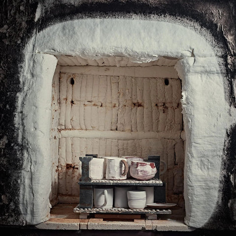 Ceramic fiber insulation blanket installed inside a kiln; white lining and mugs on a two-tier rack