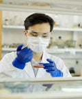 Blue nitrile medical examination gloves worn by a lab researcher, safety goggles and mask visible
