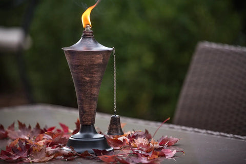 Oahu Tiki Style Outdoor Torch with brushed bronze finish, lit with flame, on deck surrounded by autumn leaves.