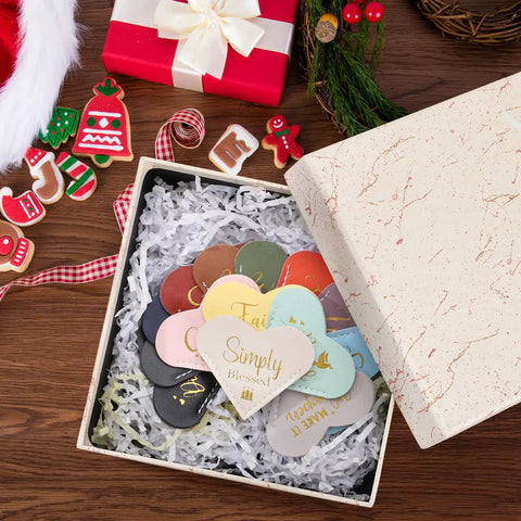 Fourteen Genuine Leather Heart Bookmarks With Uplifting Bible Verses set in a gift box with shredded paper, featuring various colors.