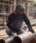 Person wearing Kick Butt Split Cowhide Leather Welding Cape Sleeve Short Jacket welding metal pipes outdoors.