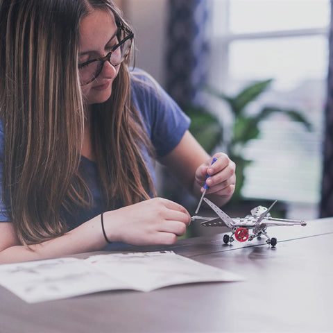 Person assembling Build Your Own Fighter Jet Erector Set Metal Model Airplane Kit with Detailed Instructions on table