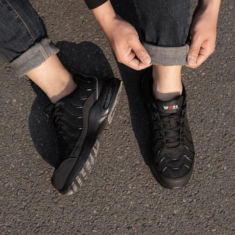Person wearing Men's Steel Toe Work Sneakers Comfortable Lightweight Safety Shoes With Breathable Mesh on asphalt