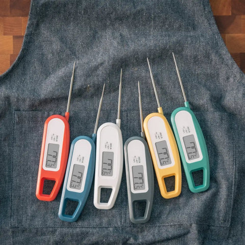 Array of ultra fast digital instant read meat thermometers with 3-4 second readouts, foldable probes on denim fabric.