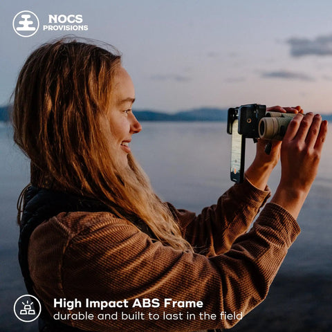 Person using Smartphone Photo Rig II Attachment for Binoculars and Telescopes at sunset, holding a phone for capturing photos.