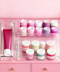 Big 26 Pack Drawer Organizer Bins In Clear Plastic, showing multiple bins with cosmetics and towels, on pink background