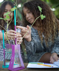 Transform Kids Into Junior Botanists With This Hella Awesome Stem Grow Kit Featuring Zero Hassle Indoor Soil Free Planting Plus Glass Flasks And Discovery Logs. Two girls examine plants in glass flasks.