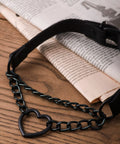 Dope Gothic Punk Leather Choker Necklace Featuring Adjustable Black Heart Chain on a wooden surface with newspaper.