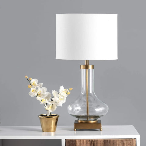 Hendry 23 Inch Glass Table Lamp with Brass Finish, Fabric Drum Shade, beside a potted orchid on a white table