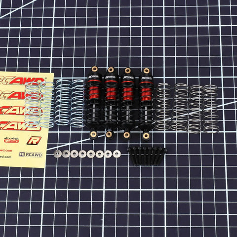 ARRMA Grom Shock Absorber Kit With 3 Spring Options, shown with red and black shocks, silver springs, and included hardware on grid.