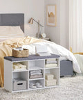 White cushioned shoe storage bench with 9 cubbies and adjustable shelves, placed in a bedroom next to a bed.