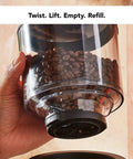 Premium Burr Coffee Grinder With Smart Dosing Technology For Dead Simple French Press To Espresso Ground Settings In Smooth Charcoal Grey Design, coffee bean container in hand.