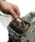 Stainless steel feeler gauge set with 32 blades (0.04–0.88 mm) used to gap spark plugs on an engine cylinder head.