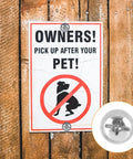 Sign on wooden fence with 'OWNERS! PICK UP AFTER YOUR PET!' and a close-up of fasteners used to secure it.