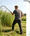 Man using Adjustable Fifty Inch Long Handle Scythe With Heavy Duty Three Section Detachable Weed Cutter And A 12.6 Inch Stainless Steel Blade for weeding.