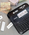 Pro Grade P-Touch PT-D610BTVP Connected Label Maker For Business And Retail on table next to printed labels and soaps