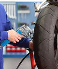 Blue KRETLAW mini grease gun with 12-inch flex hose used on motorcycle wheel in a workshop