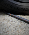 No Fuss Lightweight Hybrid Air Compressor Hose 3/8 In X 10 Ft With 1/4 Inch NPT Couplers Rated To 300 PSI beside a tire on gravel.