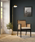 66 Inch Integrated LED Floor Lamp With Metal Shade In Brushed Brass next to a chair in a stylish dark living room.