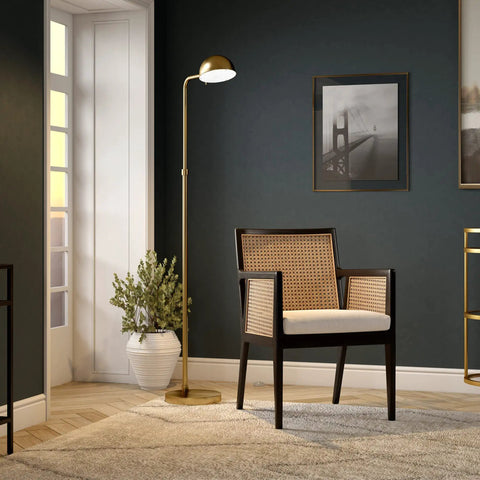 66 Inch Integrated LED Floor Lamp With Metal Shade In Brushed Brass next to a chair in a stylish dark living room.