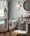 Freestanding Bamboo Coat Rack With 8 Hooks, Adjustable Height Entryway Stand For Jackets, Coats, Purses, Hats, Scarves And Umbrellas, Durable Wood And Bamboo Construction, Space Saving Organizing Solution, Classic Brown Finish in a bathroom setting next to a bathtub.